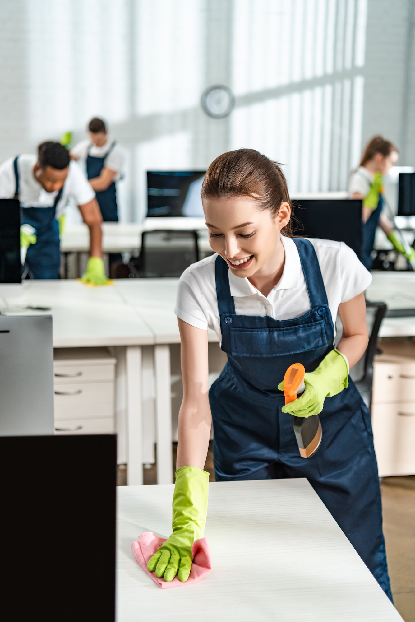 cheerful-cleaner-in-overalls-cleaning-office-desk-with-rag.jpg